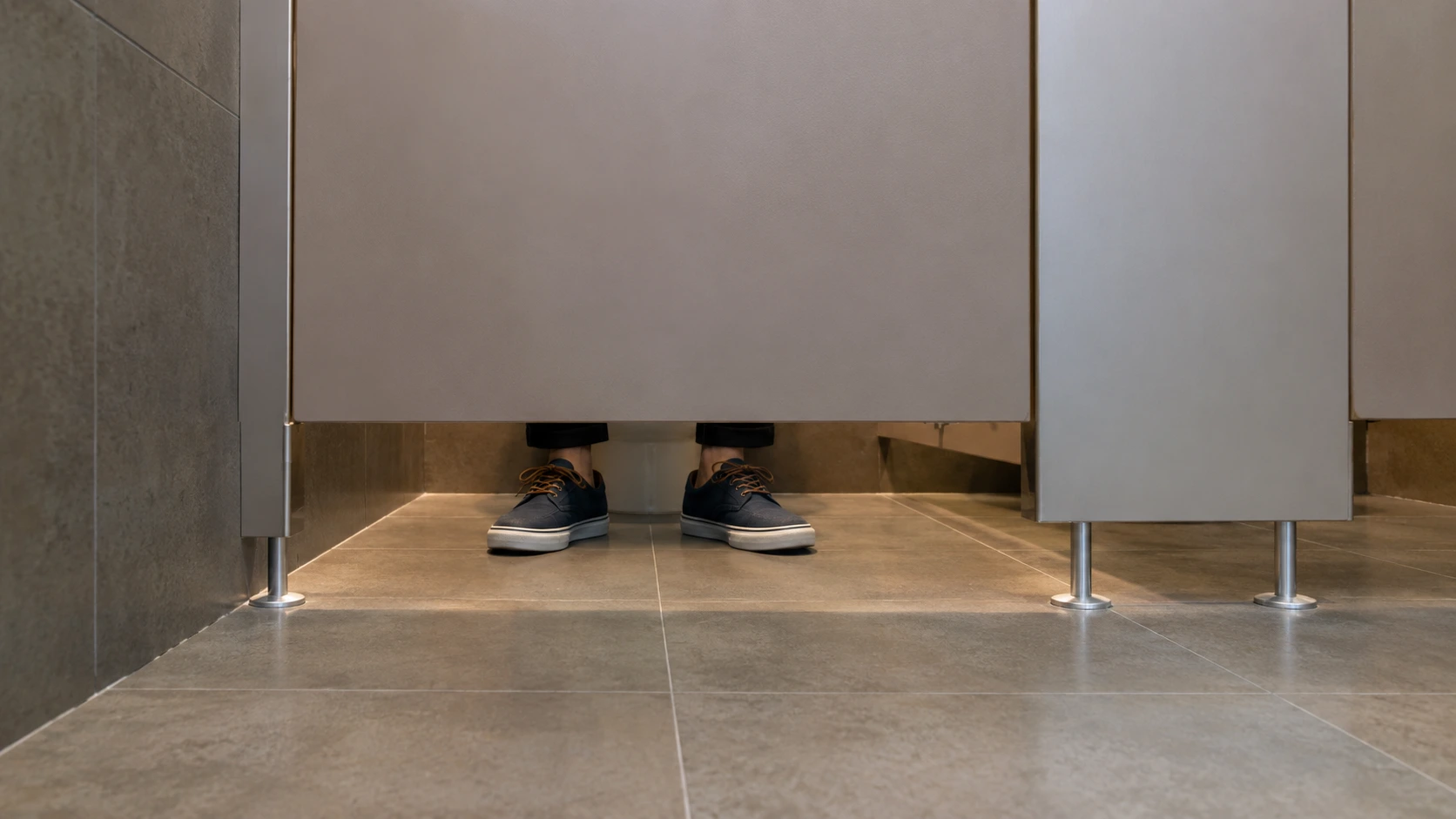 Pies visibles bajo la puerta de una cabina de baño público
